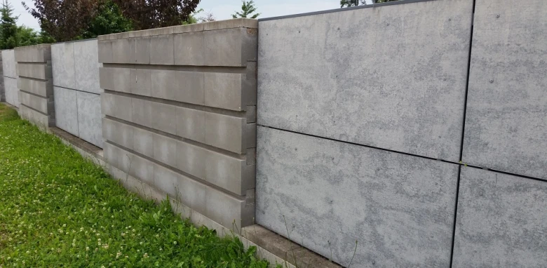 Řada šedých betonových plotů s panely instalovaných na trávníku.
