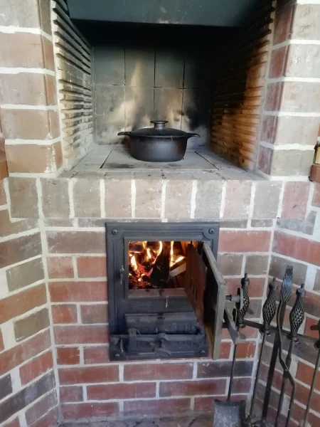 Hliněný venkovní krb s vařícím hrncem v pergole