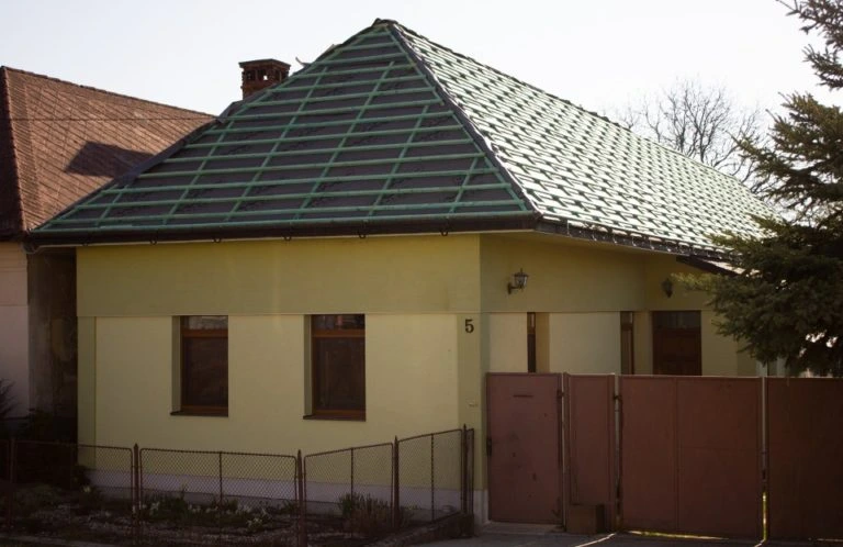 Žlutý dům s zelenou vazníkovou střešní konstrukcí.