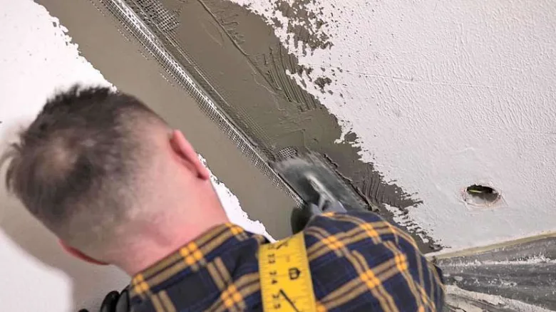 Muž lepi perlinku na stěnu špachtlí s hmotou.