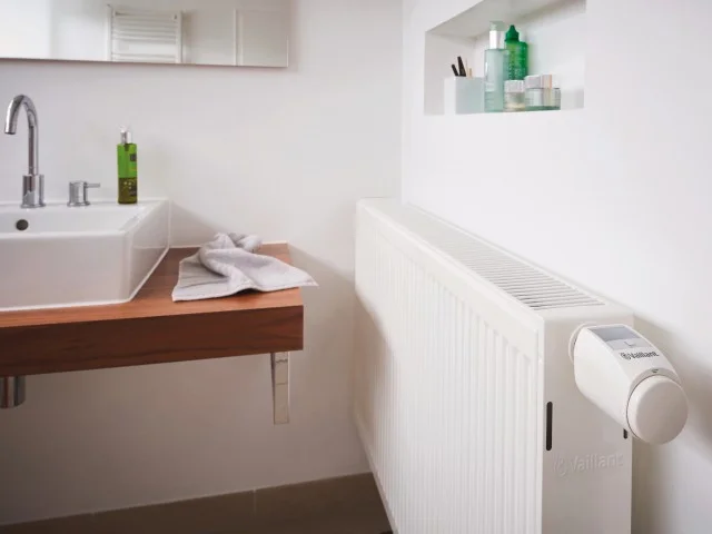 Moderní koupelna s radiátorem vybaveným elektronickým termostatem.