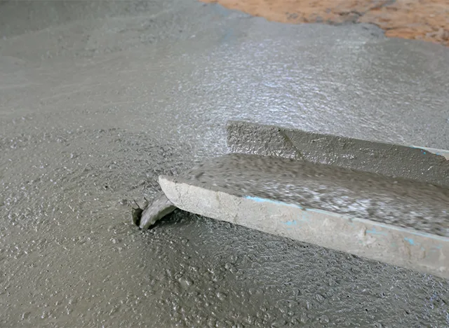 Mokrý beton se hladí dřevěným nástrojem při opravě podlahy.