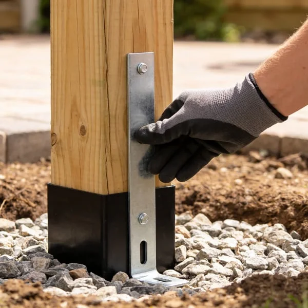 Ruční instalace kovového úchytného prvku k dřevěnému sloupu pergoly.