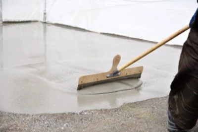 Pracovník hladí čerstvý nivelační beton na podlaze.
