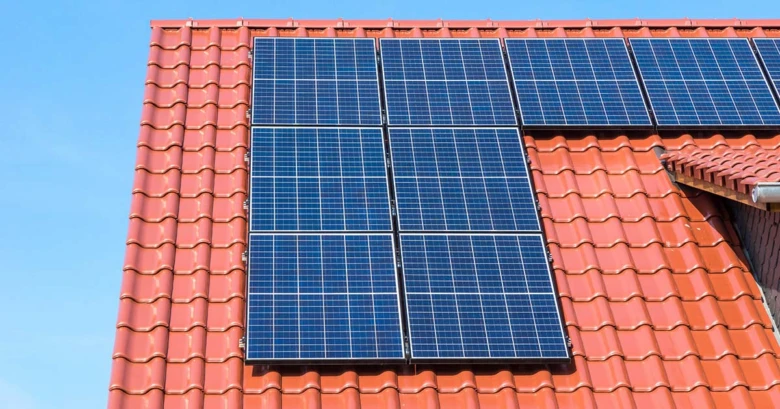 Fotovoltaické panely na červené taškové střechě domu.