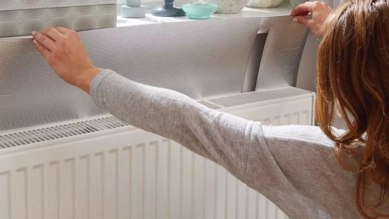 Žena aplikuje izolační síťovanou fólii na bílý radiátor.