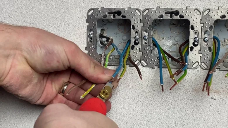 Ruční připojení vodičů do elektrické zásuvky v domácí instalaci.
