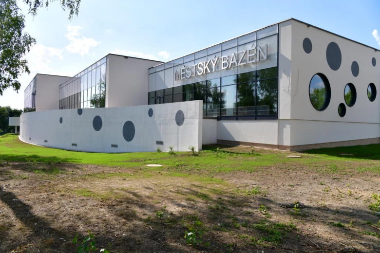 Moderní krytý městský bazén s okny a kruhovými výřezy ve fasádě.