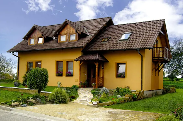 Žlutý dům s polovalbovou střechou na zelené trávníku.