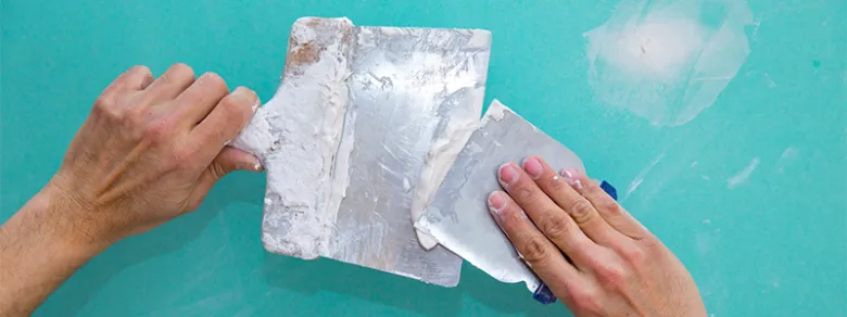 Hands applying plaster with trowels