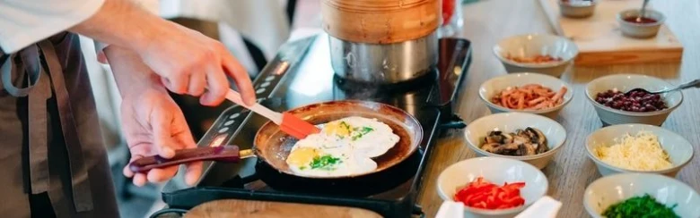 Kuchař připravuje jídlo na indukční varné desce s čerstvými ingrediencemi.