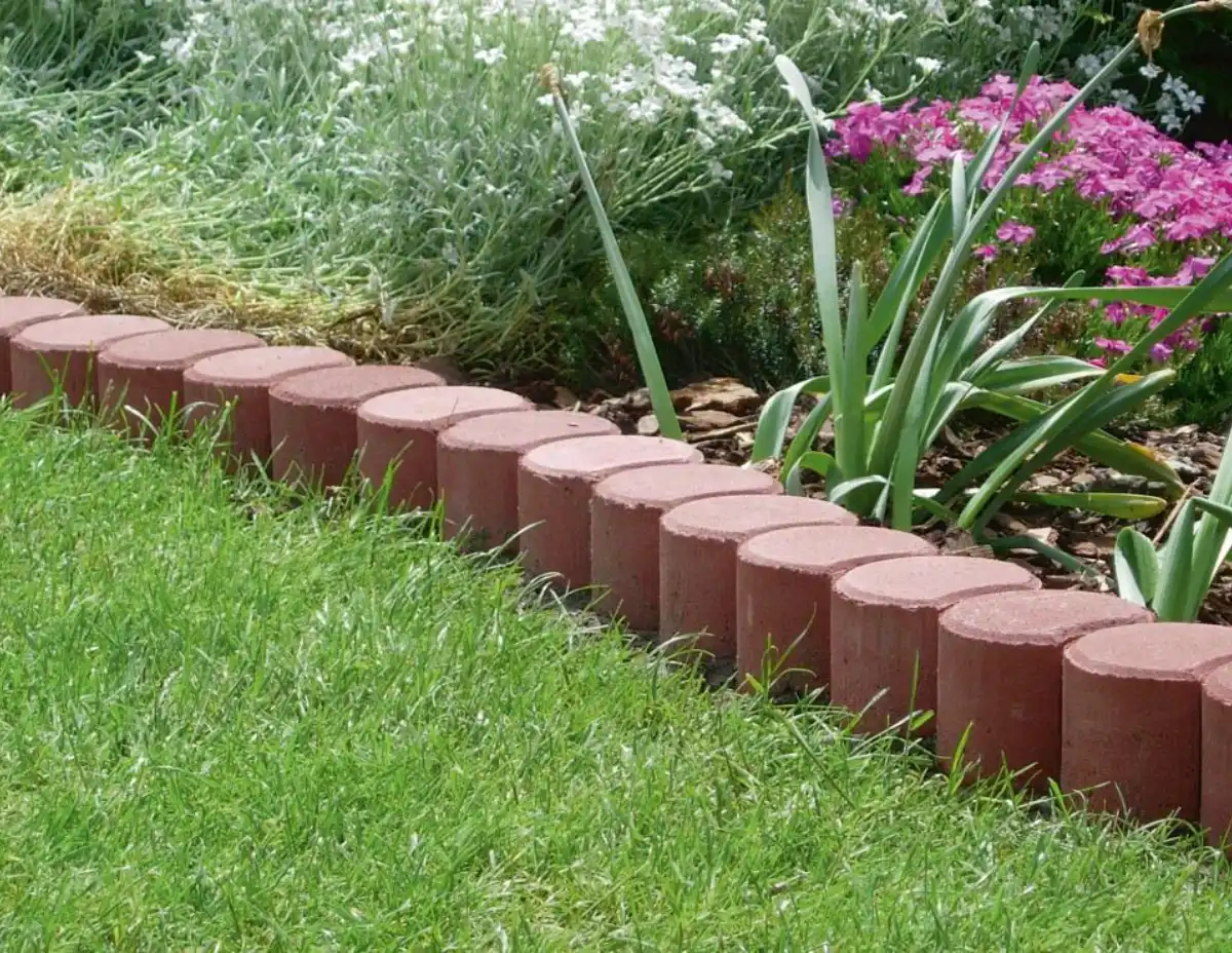 Červené betonové palisády na svahu v zahradě s kvetoucími rostlinami.