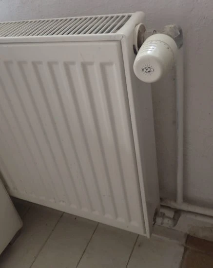 Bílý litinový radiátor s ovládacím ventilem u zdi.