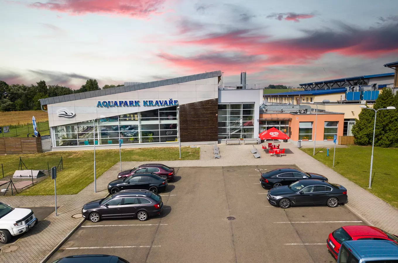 Vnější pohled na aquapark v Kravařích s parkováním aut.