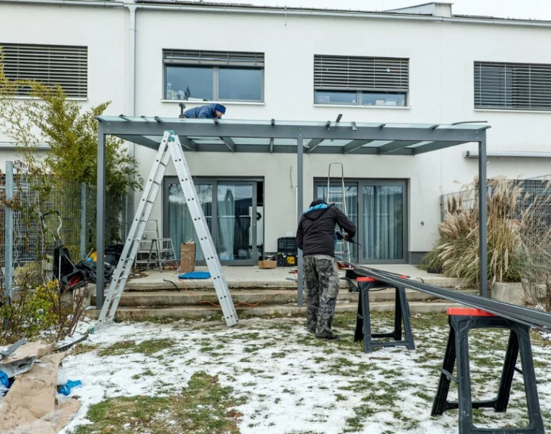 Stavba kovové pergoly u domu s pracovníky na sněhu.