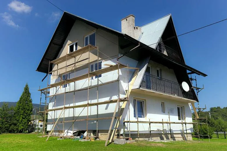 Dřevěný dům s oplocením při zateplování fasády.