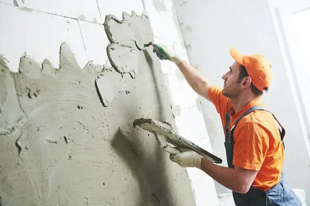 Stavebník nanáší omítku na zdi pomocí špachtle.