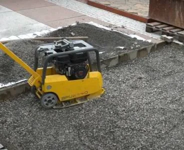 Žlutý vibrační deska na štěrku při pokládce obrubníků.