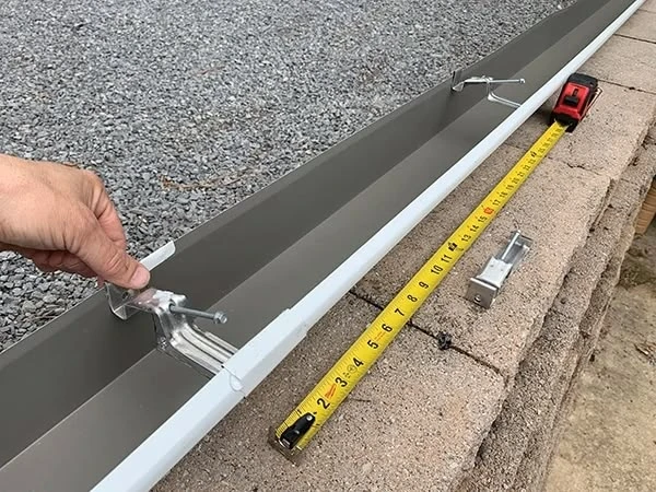 Montáž bílého okapu s držáky na betonu pomocí pásky.