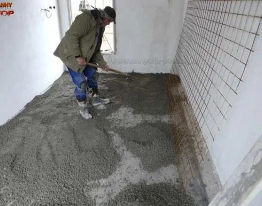 Muž nalévá beton na podlahu s instalovaným topením.