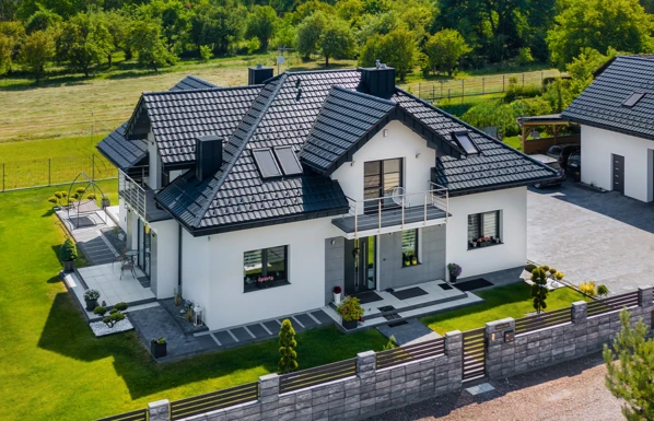 Moderní dům s tmavou keramickou střešní krytinou na pozadí zelené trávy.