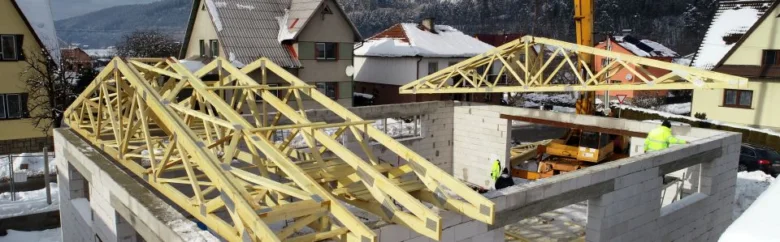 Dřevěné vazníky na střeše během stavby domu v zimním prostředí.