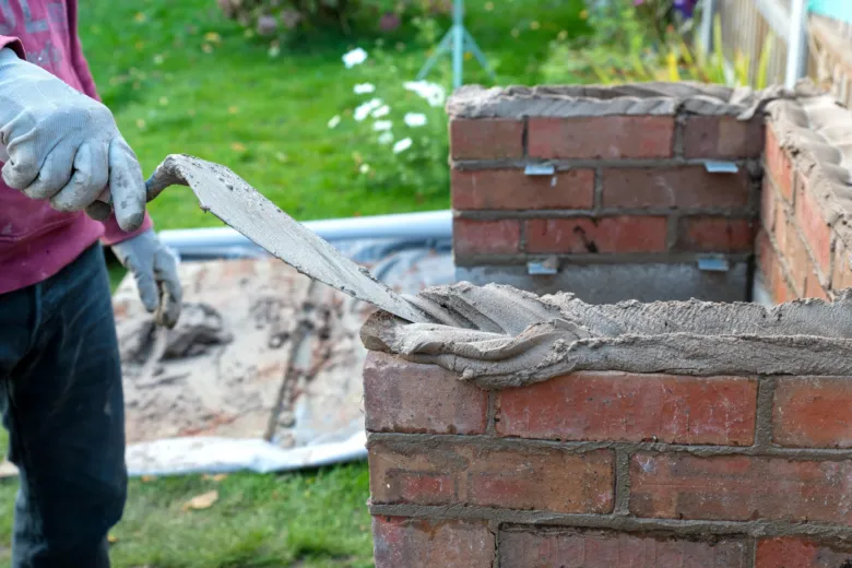 Stavebník nanáší maltu na cihlovou zeď při stavbě zahradního krbu.