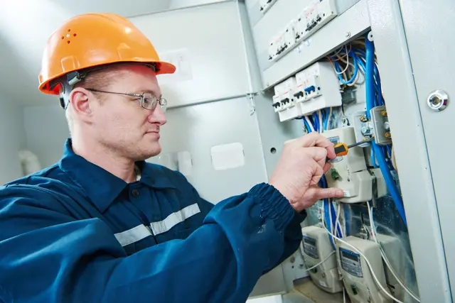 Elektrikář pracuje na průmyslovém rozvaděči v továrně.