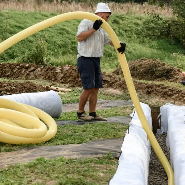 Muž instaluje žlutou drenážní hadici do přípravených zákopů pro zahradu nebo stavbu.