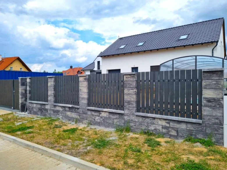 Moderní plot z pohledového betonu s tmavými lamelami u domu.
