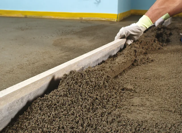 Pracovník vyrovnává čerstvý beton na hlinitém podkladu.
