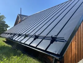 Černé trapézové plechy na dřevěné střeše v slunečním světle.