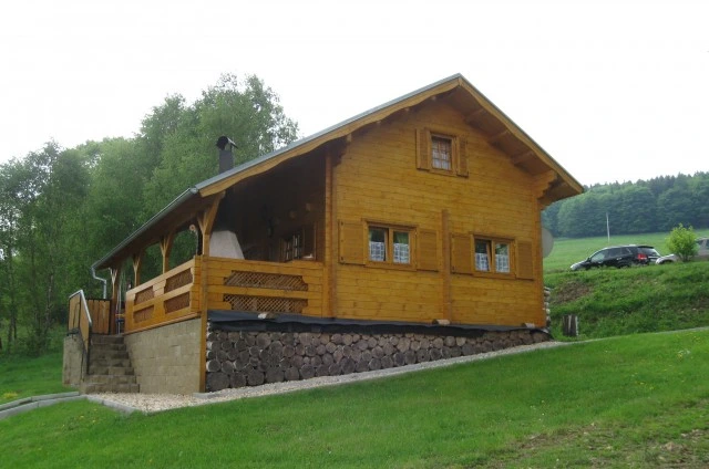 Dvoupatrová dřevěná chata na trávníku s kamenným základem.