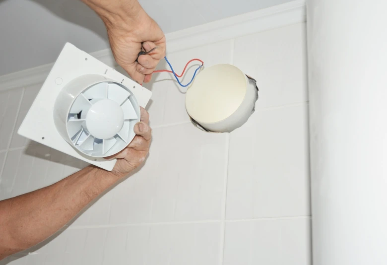 Instalace ventilátoru pro odvětrání koupelny s viditelnými kabely.