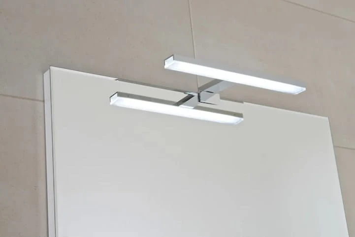 Moderní svítidlo nad zrcadlem v koupelně s bílým skříňkem.