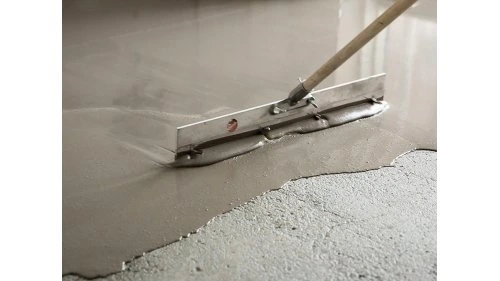 Práce s samonivelačním stěrkem pomocí špachtle na podlaze.