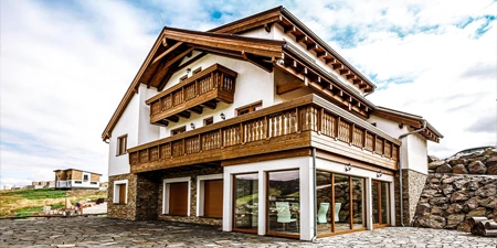 Moderní dřevostavba s balkony a velkými okny na pozadí oblohy.