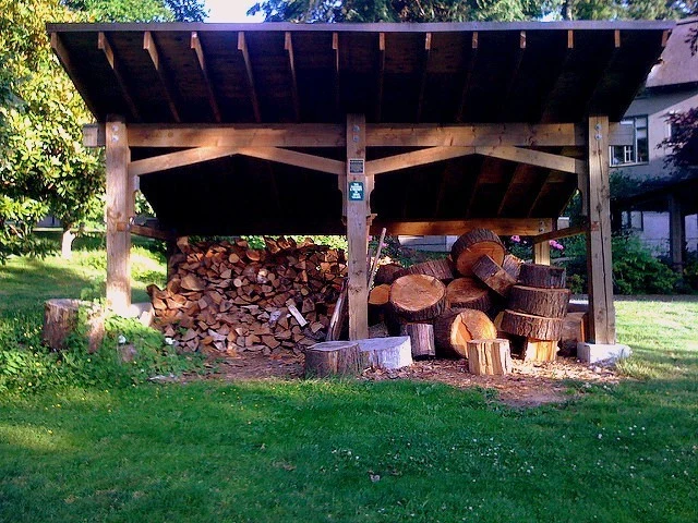 Dřevník s naskládaným palivovým dřívím pod střešní konstrukcí.