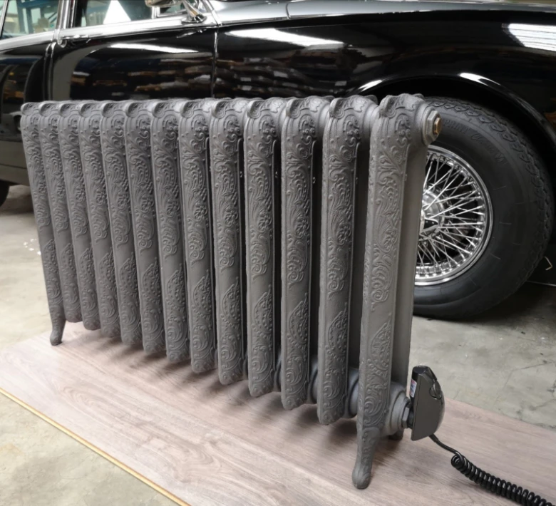 Detailní litinový radiátor s dekorativním vzorem umístěný vedle starého vozu.