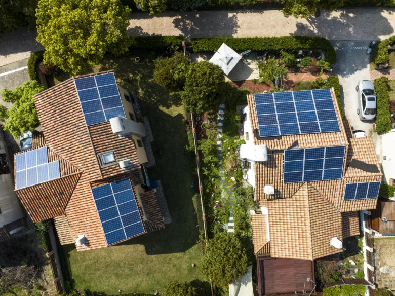 Dvě domy s fotovoltaickými panely na střechách zobrazené ze vzduchu.