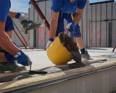 Stavební dělnici nalévají čerstvý beton na dřevěné podlahy.