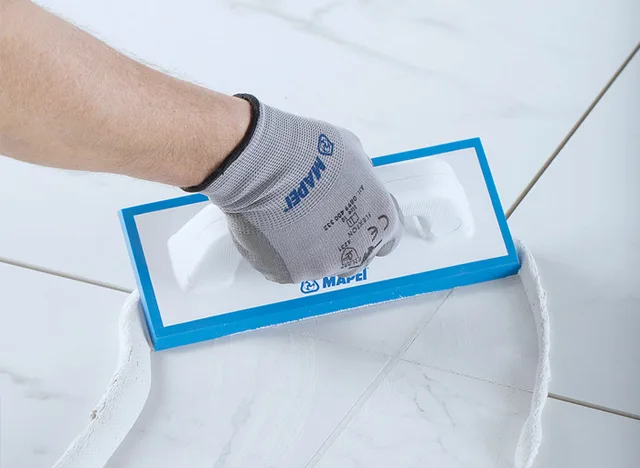 Ručník s hřebenem nanáší hydroizolační směs na dlažbu v koupelně.