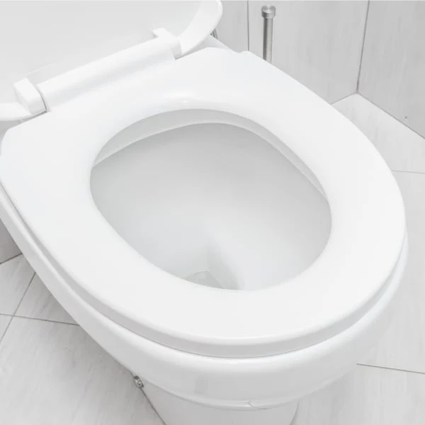 Bílá toaletní sedátko s miskou na světlém dlaždicovém podlaze.