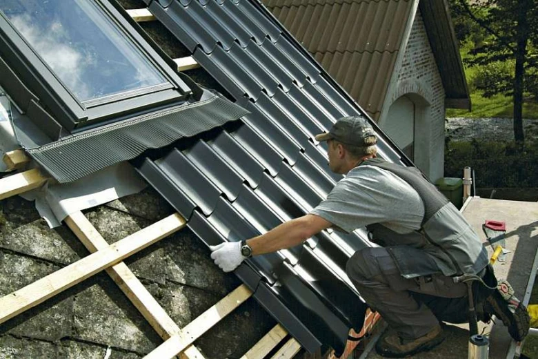 Stavebník montuje tmavě šedý falcovaný plech na střešní konstrukci.