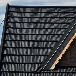 Detail tmavých plechových střešní krytin s hřebenovou šablonou.