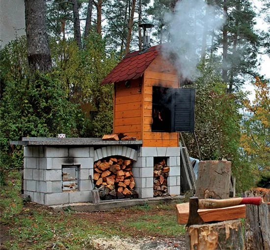 Samostatně postavená dřevěná udírna s kamenným základem v lese.