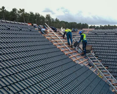 Montáž dřevěných krokví na střeše s pracovníky v ochranném oblečení.