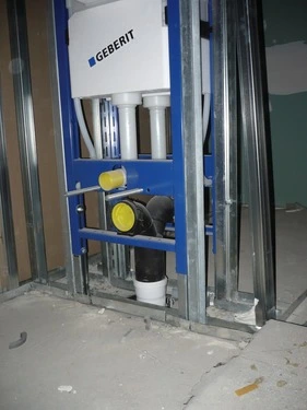 Skrývaná nádrž Geberit s připojenými vodovodními a odpadními trubkami v koupelně.