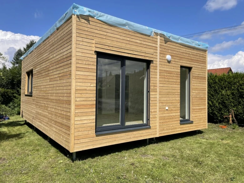 Moderní dřevěný modulární dům na trávníku pod modrou oblohou.