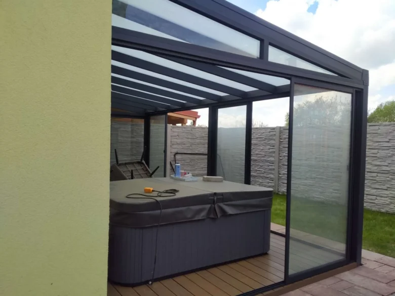 Skleněná pergola s plexisklem obklopující horkou vany na dřevěné terase.